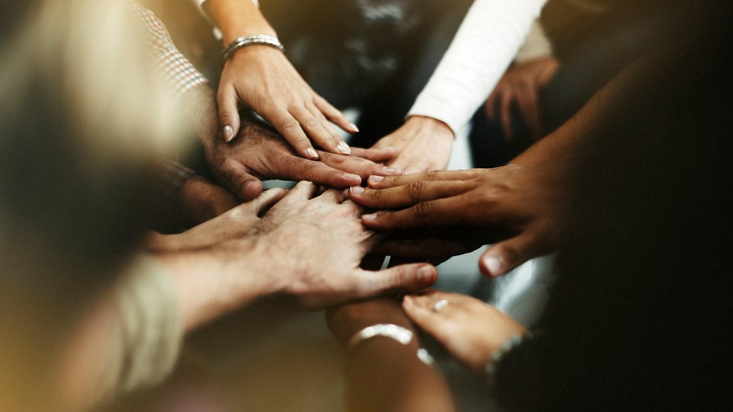 Diverse Hands Together in Unity A group of diverse hands stacked together, symbolizing teamwork and collaboration among individuals from various backgrounds.